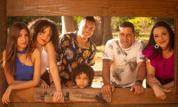 A family enjoying a sunny day together outside a rustic cabin window, smiling warmly.